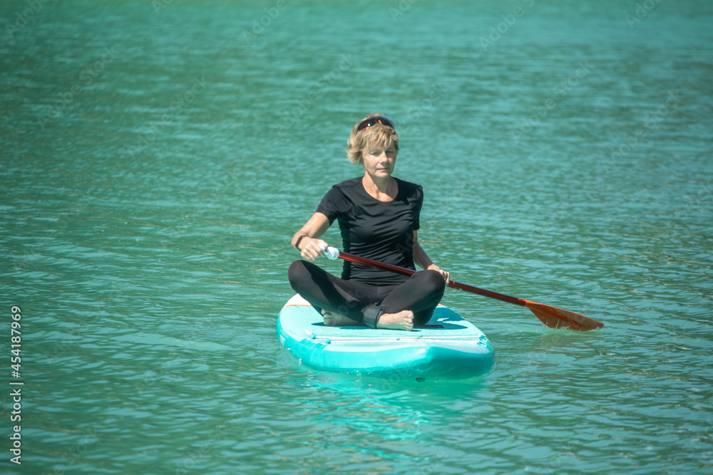 SUP concept surfboard - cute young woman is paddling on a beautiful lake with turquoise water