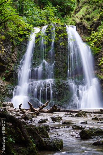 Ein imposanter Wasserfall mitten im Wald. Das Wasser flie  t in einen Fluss. Es gibt B  ume rund um den Wasserfall.