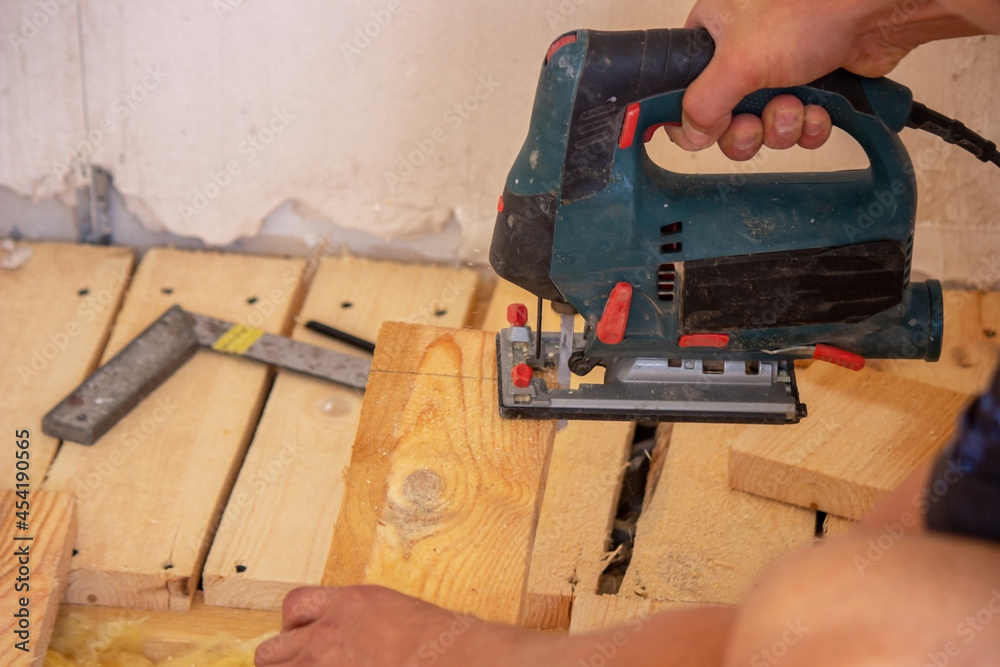 A man cuts a board with an electric saw. Repair of the floor in the house. Selective focus.