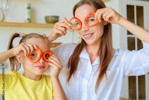 Mother and child preparing healthy food and having fun, holds a pepper in front of their eyes like a glasses