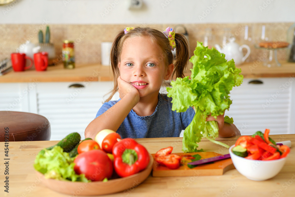 Adorable child is cooking in the kitchen. Pretty pretty girl prepares soup. Little chef preparing healthy food vegetable salad