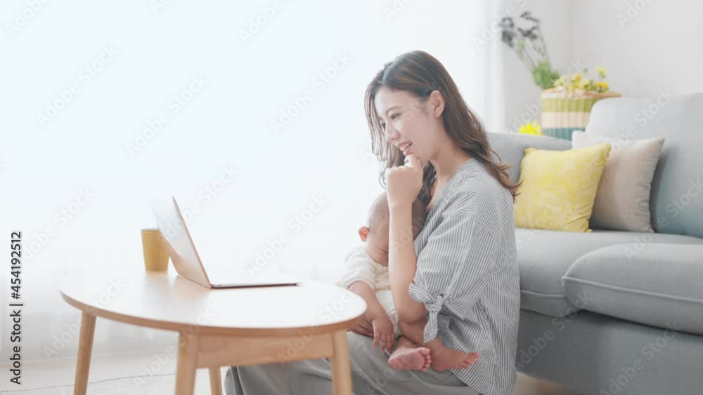 赤ちゃんを抱きながらノートパソコンを使う母親 赤ちゃんを抱きながらノートパソコンを使う母親