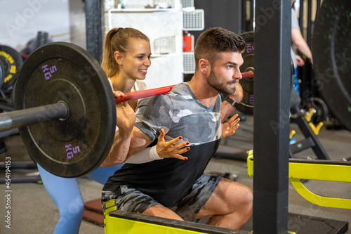 Female personal fitness trainer assisting a muscular man working out with heavy barbells. Sport, fitness, teamwork, weightlifting and people concept.