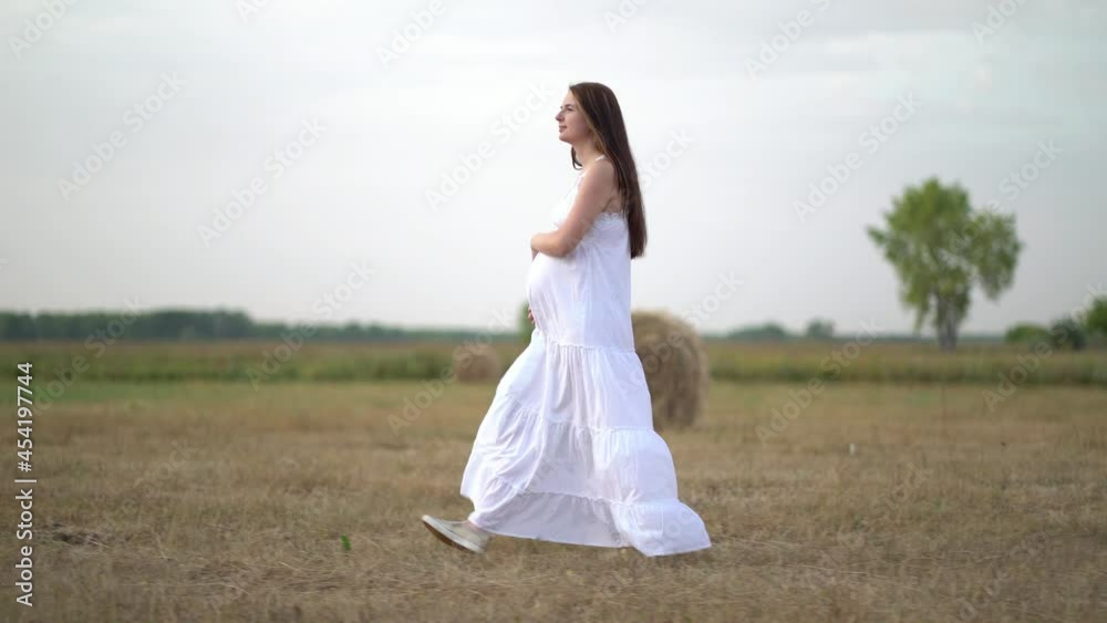 Beautiful pregnant woman in wheat field with haystacks at summer day