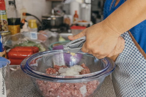 Hispanic mother seasoning raw gound meat with squeezed garlic photo