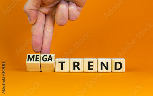 Trend or megatrend symbol. Businessman turns wooden cubes and changes words trend to megatrend. Beautiful orange table, orange background, copy space. Business, trend or megatrend concept. photo