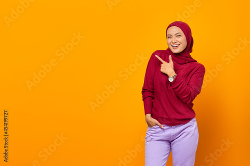 Cheerful asian woman pointing fingers to empty space over yellow background © Bangun Stock Photo
