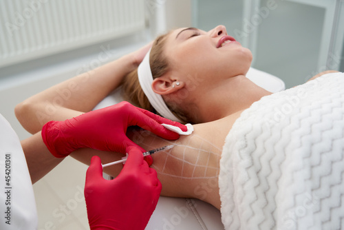 Doctor makes injections of botulinum toxin in the underarm area against hyperhidrosis in beauty salon. Female cosmetology and problems with sweating concept photo