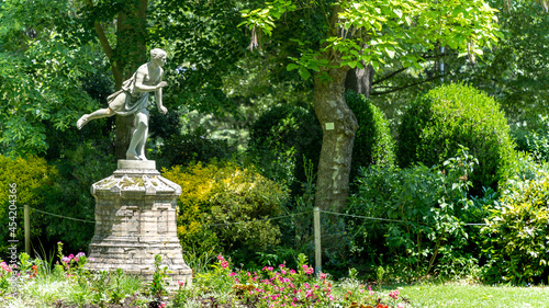 Statue of an ancient person slender on one foot, surrounded by lush plants and trees 