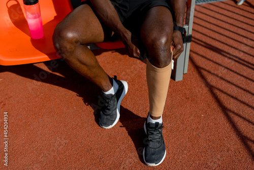A male African American track and field athlete sits on a bench puts on a sports stocking before the race
