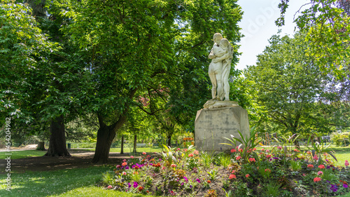 Pretty statues of a hugging couple, surrounded by trees and flowers 