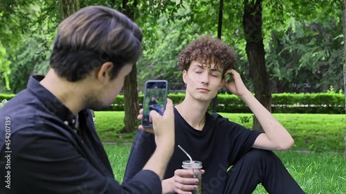A guy takes pictures on the phone of another guy in nature in the summer