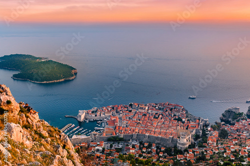 Group of young adults sit on cliff side looking down at Dubrovnik ity during sunset