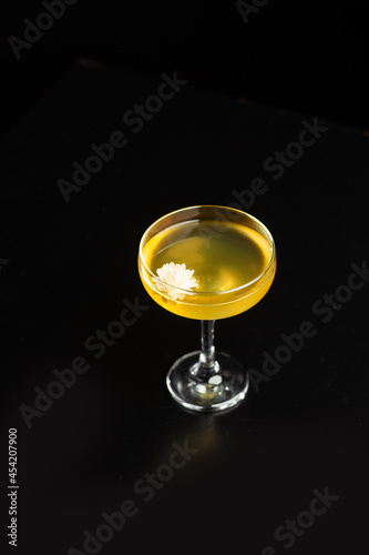 Glass with yellow lemon cocktail on the bar on a black background. the drinks is decorated with flower