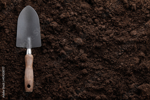 Garden trowel on soil background, close up view photo