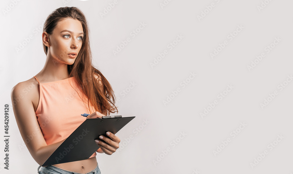 Girl student writes information. Beautiful young business woman isolated on gray background. Achieving career wealth business concept. Mockup copy space. Hold a clipboard with documents