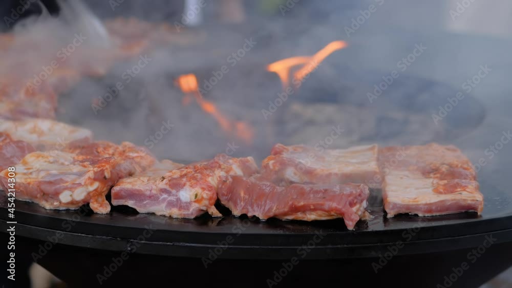 Slow motion: process of cooking fresh juicy meat steaks on round brazier with hot flame at summer local food market - close up view. Outdoor cooking, gastronomy, cookery, street food concept Slow motion: process of cooking fresh juicy meat steaks on round brazier with hot flame at summer local food market - close up view. Outdoor cooking, gastronomy, cookery, street food concept