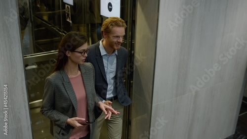 Businessman and businesswoman talking in lift car. Colleagues exiting elevator