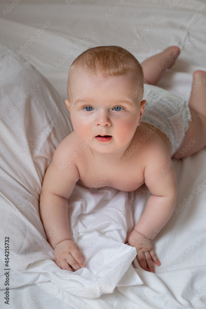 a cute baby is lying in diapers in a bed with white cotton bed linen. High quality photo a cute baby is lying in diapers in a bed with white cotton bed linen. High quality photo