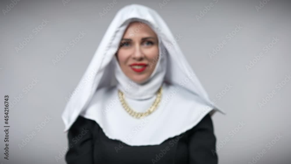 Close-up female hands making heart shape with blurred Caucasian woman in nun costume smiling looking at camera from background. Happy positive lady posing at grey background Close-up female hands making heart shape with blurred Caucasian woman in nun costume smiling looking at camera from background. Happy positive lady posing at grey background