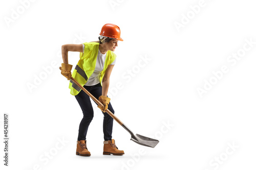 Obraz na plátně Female worker wearing a hardhat and a tool belt digging with a shovel