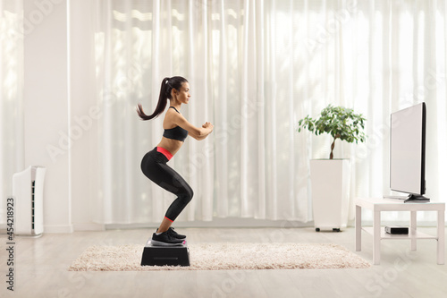 Full length profile shot of a young woman exercising step aerobic in front of tv