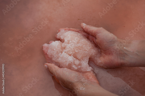 Women's hands hold pink salt at surface of water of a unique pink lake. Original color of lake is given by halophilic microalgae Dunaliella salina. Pink salt is used in cosmetology and folk medicine photo