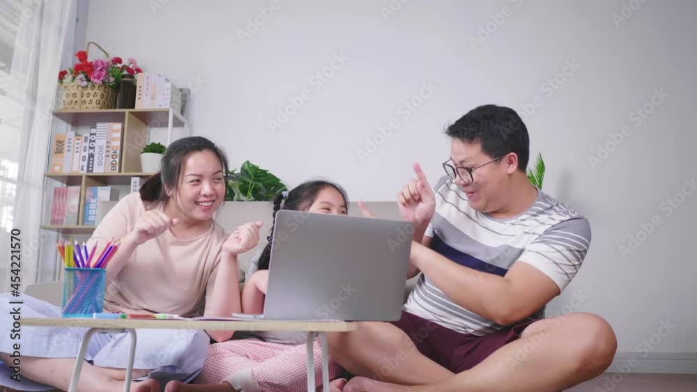 Happy Asian family sitting on the floor in living room and dancing together. Putting laptop on the table. Daughter, mom and dad. Happy family concept Happy Asian family sitting on the floor in living room and dancing together. Putting laptop on the table. Daughter, mom and dad. Happy family concept
