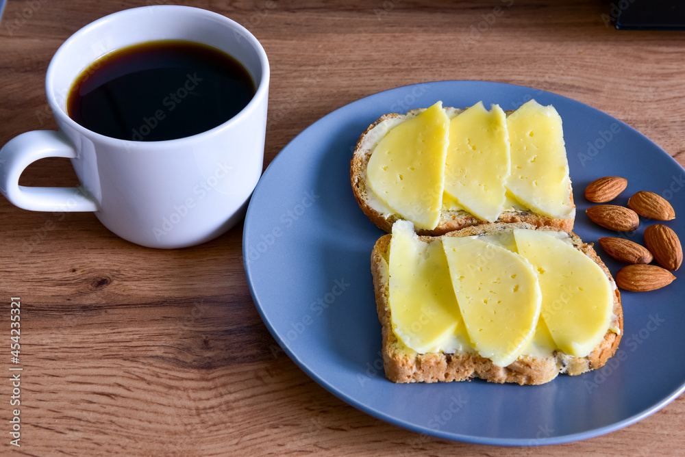 A cup of coffee, toast with cheese and almonds on a plate, stand on a wooden table