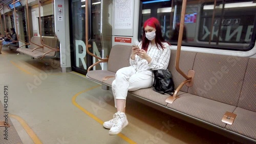 Moscow, Russia August 25, 2021 Beautiful red-haired student girl in subway in covid19 face mask and chatting on smartphone in social networks.Viral infection pandemic influenza coronavirus 2019-ncov