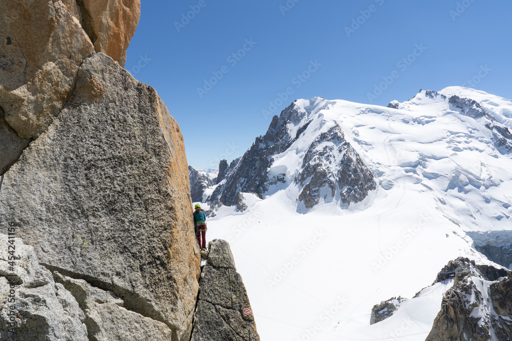 A panoramic view of European Alps on a sunny day. Mount Blanc as a highest mountain in Europe covered with snow and glacier. A climber on a rock