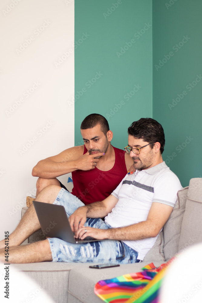 Fototapeta premium beautiful gay couple sitting on the sofa looking for something on the internet