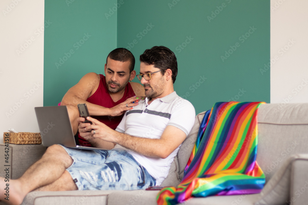 beautiful gay couple sitting on the sofa looking for something on the internet beautiful gay couple sitting on the sofa looking for something on the internet