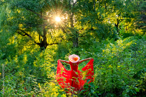A lady in red dress is walking and dancing in forest under the sunlight