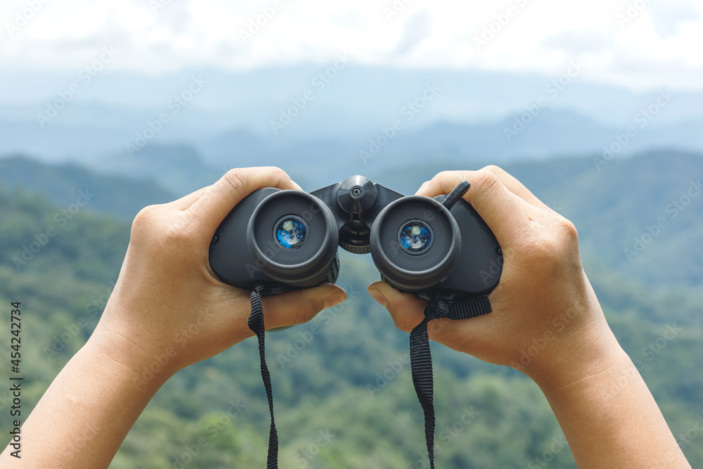 Hands holding binoculars on mountains background Hands holding binoculars on mountains background