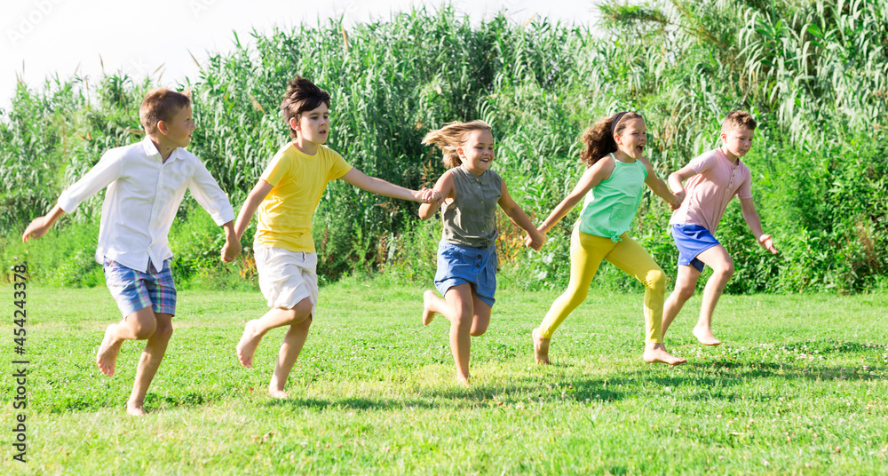 Happy active children running together on green grass in park