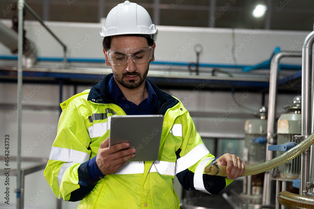 Male factory mechanic wearing safety glasses, white helmet. Technicians male working with digital tablet, checking the operation of equipment, repairing and maintenance machinery in industry factory Male factory mechanic wearing safety glasses, white helmet. Technicians male working with digital tablet, checking the operation of equipment, repairing and maintenance machinery in industry factory