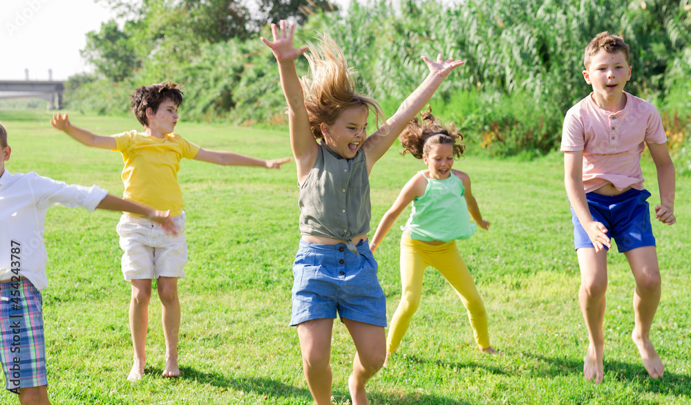 Group of children, boys and girls, jumping together on green grass in a park on sunny day