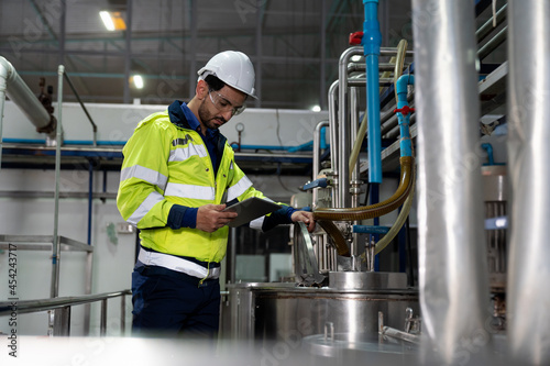 Male factory mechanic wearing safety glasses, white helmet. Technicians male working with digital tablet, checking the operation of equipment, repairing and maintenance machinery in industry factory