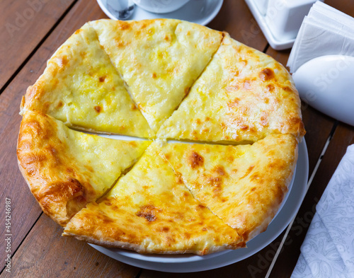 Georgian delicious flatbread khachapuri Iveria, covered with suluguni cheese, cut into pieces on a plate