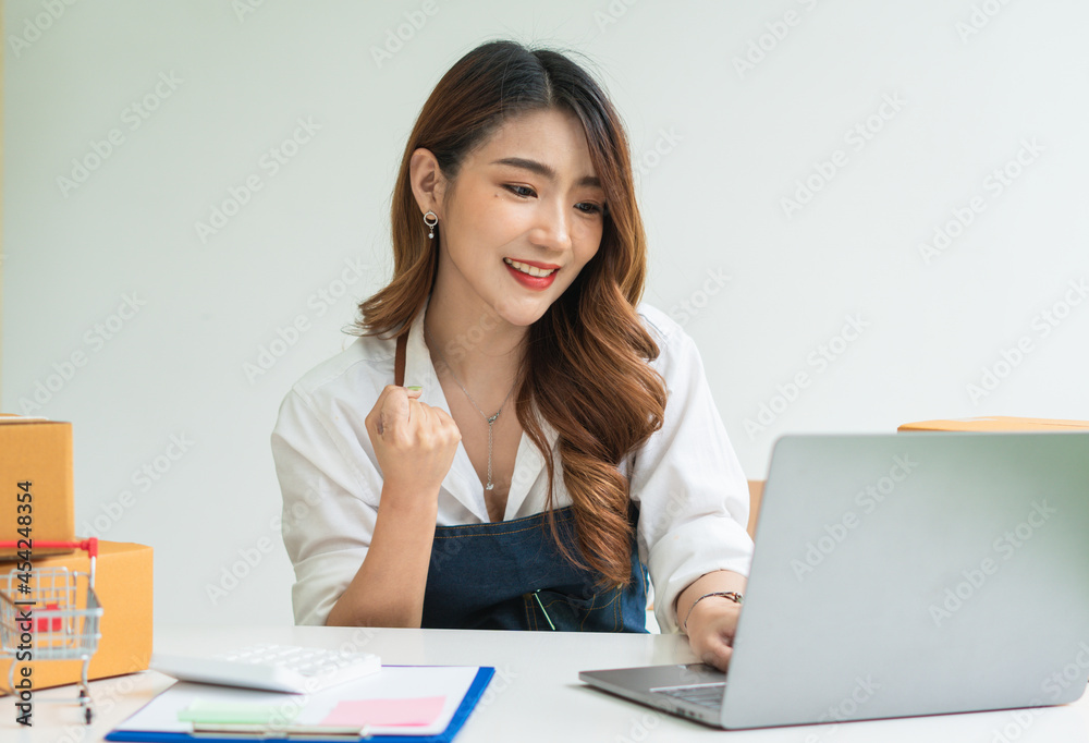 Young smiling beautiful owner asian woman freelance sme business online shopping working on laptop computer with parcel box on desk at home - SME business online and delivery concept Young smiling beautiful owner asian woman freelance sme business online shopping working on laptop computer with parcel box on desk at home - SME business online and delivery concept