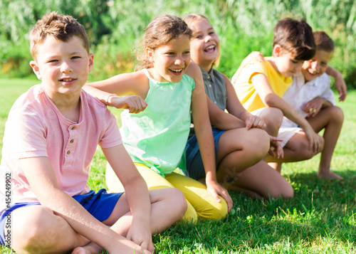 Canvas-taulu Schoolchildren sitting on grass during sunny summer day.