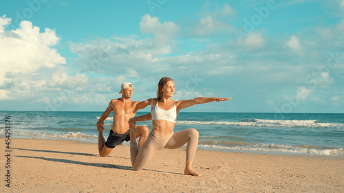 Couple training - Young sports couple doing acro yoga exercises on sand beach. Couple making yoga exercises on sand. fitness, sport, people and lifestyle concept, Caucasian fitness model.