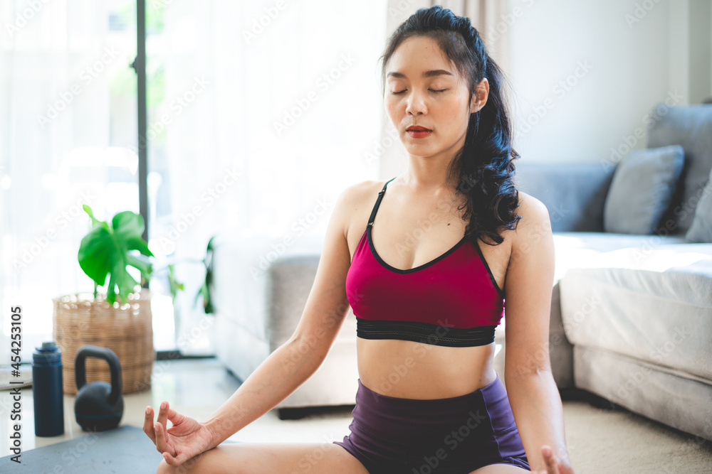 young Asian woman exercise by yoga at home gym, healthy female lifestyle with fitness sport training at home, girl doing body active physical exercise indoor house room, relaxation and wellness