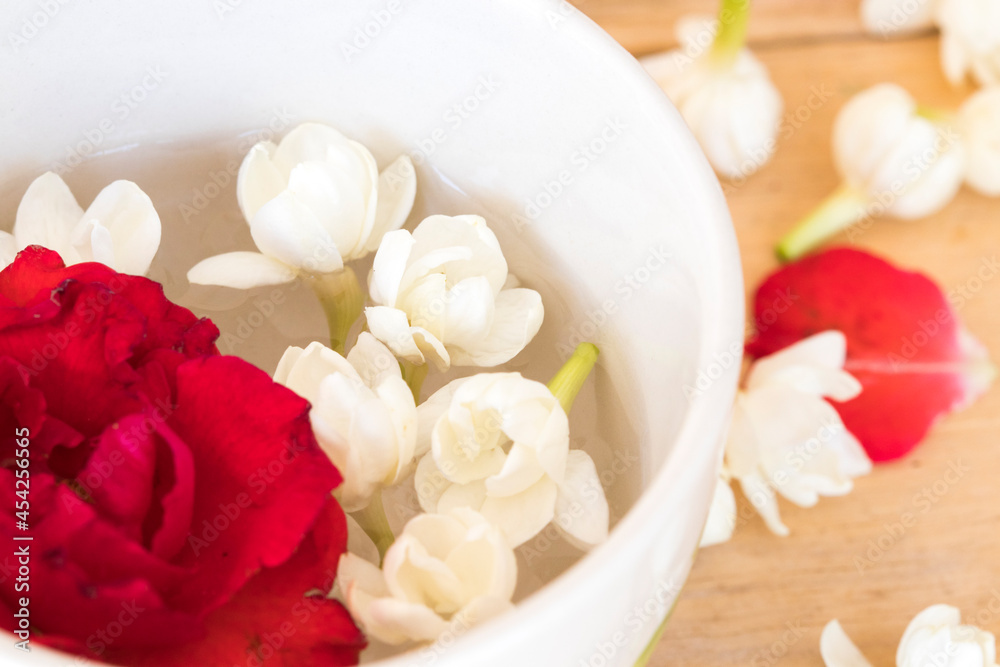 rose, jasmine flowers float on water in cup arrangement flat lay style on background wooden