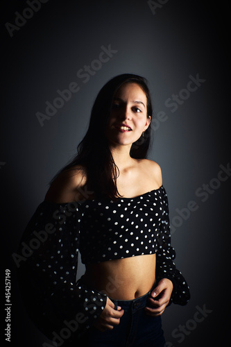Close-up portrait of a young woman with a positive gaze looking at the camera, on a dark studio background