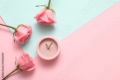 Alarm clock with rose flowers on color background
