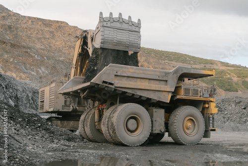 Excavator loads ore to a dump truck. The action takes place in an open pit.