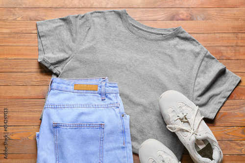Stylish t-shirt, jeans and shoes on wooden background