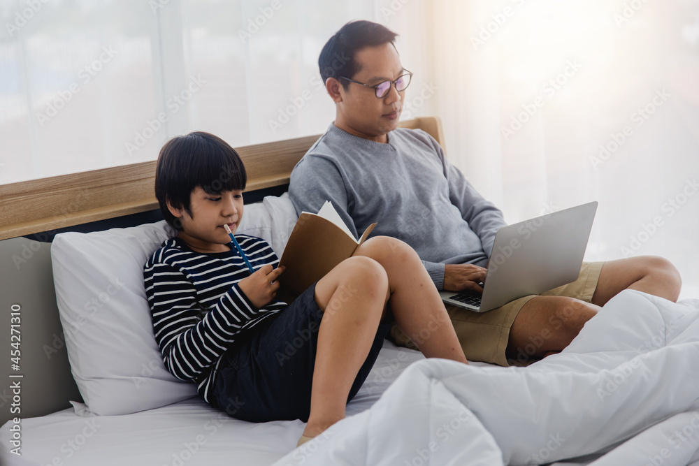 Father and son with laptop  next to his little son do home work on bed at home